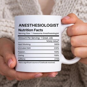 May include: White ceramic coffee mug with a black and white graphic of a nutrition facts label for an anesthesiologist. The label lists the daily value of hard working, unrivaled skill, passion, caring, and caffeine.