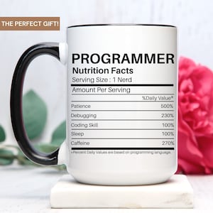May include: White ceramic mug with a black handle. The mug has a black rim and features a graphic of a nutrition facts label for a "Programmer". The label lists the daily value of patience, debugging, coding skill, sleep, and caffeine.