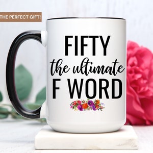 May include: White ceramic coffee mug with a black handle and black rim. The mug has the text "FIFTY the ultimate F WORD" in black lettering with a floral design below the text.