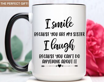 May include: White ceramic coffee mug with a black handle and black rim. The mug has black text that reads "I smile because you are my sister I laugh because you can't do anything about it" with arrows and a heart.
