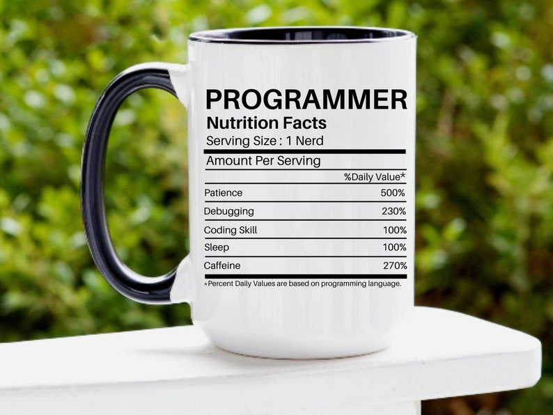 May include: White ceramic mug with a black handle and rim. The mug features a black and white graphic that reads "PROGRAMMER Nutrition Facts Serving Size: 1 Nerd Amount Per Serving %Daily Value* Patience 500% Debugging 230% Coding Skill 100% Sleep 100% Caffeine 270% *Percent Daily Values are based on programming language."