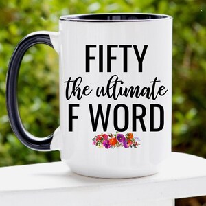 May include: White ceramic coffee mug with a black handle and rim. The mug has black text that reads "FIFTY the ultimate F WORD" with a floral design below the text.