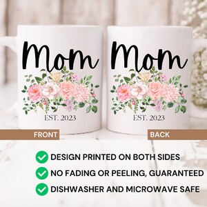 May include: White ceramic mug with a floral design and the word "Mom" printed in black. The text "EST. 2023" is printed below the floral design. The mug is shown from the front and back.