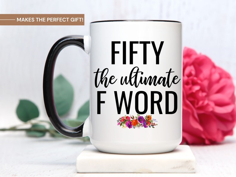 May include: White ceramic coffee mug with a black handle and black rim. The mug has the text "FIFTY the ultimate F WORD" in black lettering with a floral design below the text.