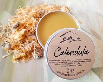 May include: A small tin of Calendula salve with a brown label. The label has a mountain range illustration and the text "Calendula", "wildcrafted pinyon pine sap", "organic calendula flowers", "wildcrafted willow bark", "beeswax", "organic olive oil", "grapeseed oil", "tea tree & lavender essential oils", "2 oz.", and "www.ROCKY MOUNTAIN HERBS.CO".