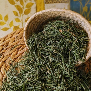 May include: A woven basket filled with a large amount of green pine needles. The basket is sitting on top of a woven mat.