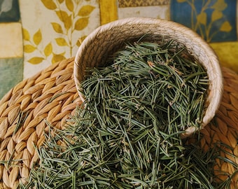 May include: A woven basket filled with a large amount of green pine needles. The basket is sitting on top of a woven mat.