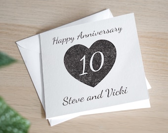 May include: A white card with the text "Happy Anniversary" and a black heart with the number "10" inside. The text "Steve and Vicki" is below the heart.