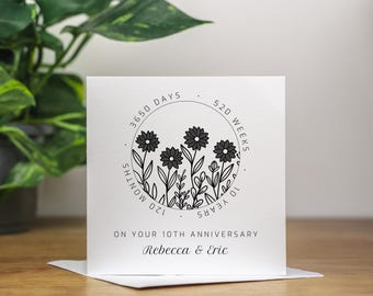 May include: A white card with black text and a black and white illustration of flowers in a circle. The text reads "3650 days, 520 weeks, 120 months, 10 years" and "On your 10th Anniversary, Rebecca & Eric".