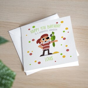 May include: A birthday card featuring a cartoon pirate and parrot illustration. The card reads "Happy 9th Birthday to a Wonderful Grandson" with the name "Louis" below. The design includes colourful polka dots, and the card is inside a white envelope.