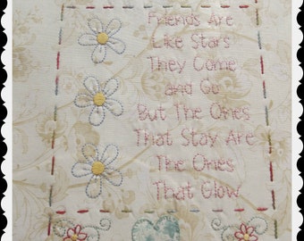 May include: Embroidered white fabric with a quote about friendship: "Friends are like stars. They come and go, but the ones that stay are the ones that glow." The quote is surrounded by embroidered flowers and a heart.