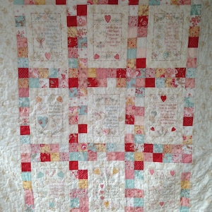 Może przedstawiać: Kołdra w patchworkowym wzorze z czerwonymi, różowymi i niebieskimi kwadratami. Kołdra jest ozdobiona haftowanymi sercami i cytatami o przyjaźni, w tym "Przyjaciel to ten, kto wierzy w ciebie, gdy przestałeś wierzyć w siebie." i "Ramię w ramię lub oddaleni o wiele kilometrów, przyjaciele są na zawsze blisko serca."