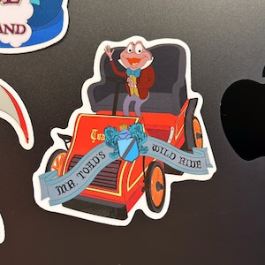 May include: A red and blue sticker featuring a cartoon frog driving a red car with the text "Mr. Toad's Wild Ride".