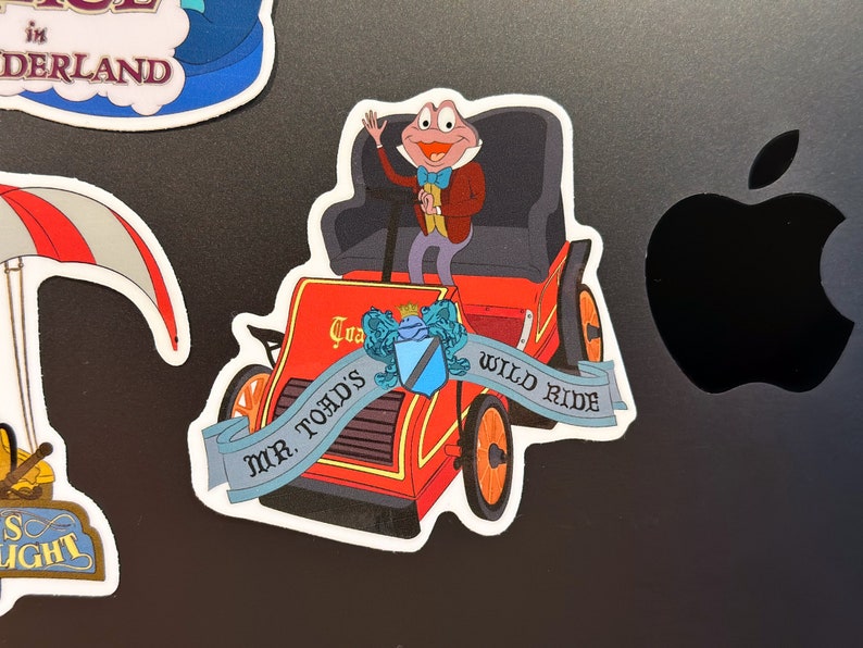 May include: A red and blue sticker featuring a cartoon frog driving a red car with the text "Mr. Toad's Wild Ride".