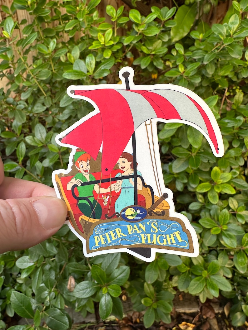 May include: A sticker featuring Peter Pan and Wendy flying in a red and white boat with the text "Peter Pan's Flight".