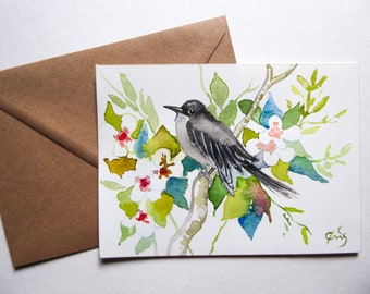 Könnte beinhalten: Aquarellmalerei eines Vogels, der auf einem Ast mit weißen Blüten, grünen Blättern und roten Akzenten sitzt. Der Vogel hat graue und schwarze Federn. Ein brauner Umschlag befindet sich im Hintergrund. Das Kunstwerk ist unten rechts signiert.