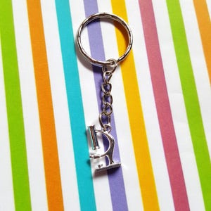 May include: A silver microscope keychain with a silver ring and chain. The keychain is on a background of colorful stripes.
