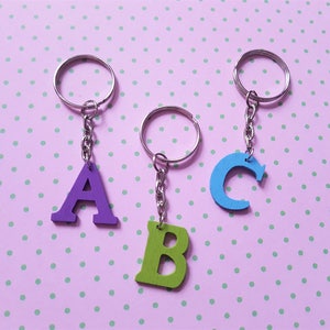 May include: Three wooden letter keychains, each with a different letter of the alphabet. The letters are A, B, and C. The keychain with the letter A is purple, the keychain with the letter B is green, and the keychain with the letter C is blue.