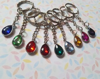 May include: A set of eight keychains with teardrop-shaped crystal charms in various colors, including blue, green, red, orange, pink, and purple. The keychains are made of silver metal.