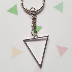 Può includere: Un portachiavi a forma di triangolo argentato con un anello e una catena argentati. Il triangolo ha uno spazio vuoto all'interno.