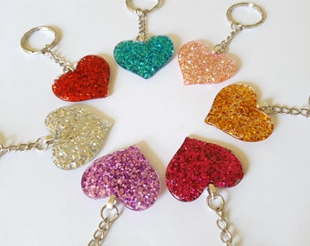 May include: Seven heart-shaped keychains with glitter embedded in clear resin. The keychains are in the colors red, pink, silver, purple, teal, gold, and burgundy.