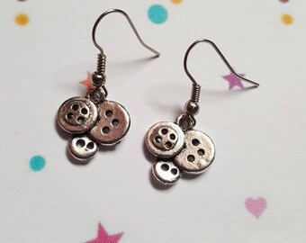 May include: A pair of silver button earrings with three buttons on each earring. The buttons are stacked on top of each other and have a slightly raised design.