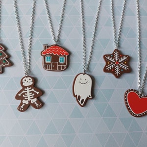 May include: Six gingerbread-themed necklaces with different charms, including a gingerbread house, a snowflake, a ghost, a skeleton, a heart, and a Christmas tree.
