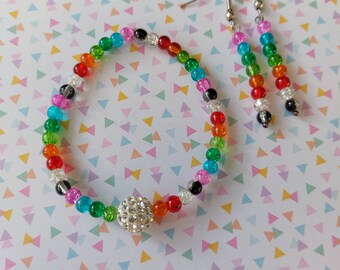 Op de afbeelding: Een kleurrijke kralen armband met een grote strass bedel en bijpassende oorbellen. De kralen zijn veelkleurig en bevatten tinten rood, oranje, geel, groen, blauw en paars.