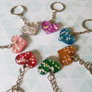 Puede incluir: Siete llaveros en forma de corazón con purpurina y detalles de estrellas. Los llaveros son de varios colores, incluyendo rosa, rojo, verde, azul, plateado, dorado y morado.