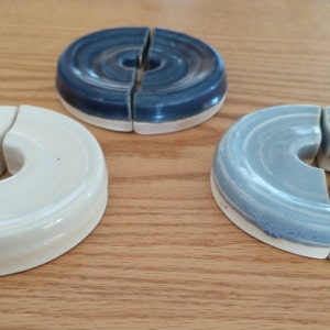 Peut inclure: Trois dessous de verre en céramique en forme de donut, dans des tons de bleu et de crème. Chaque dessous de verre est divisé en deux parties. Les dessous de verre sont disposés sur une surface en bois brun clair.