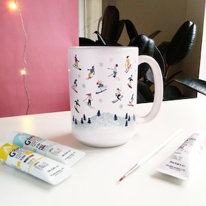 May include: White ceramic mug with a winter sports theme. The mug features a repeating pattern of skiers and snowboarders in various poses on a snowy mountain scene. The mug has a black handle and a white interior.