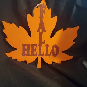 Hola otoño, en forma de hoja, naranja, con letras de óxido oscuro. Con cordel para colgar