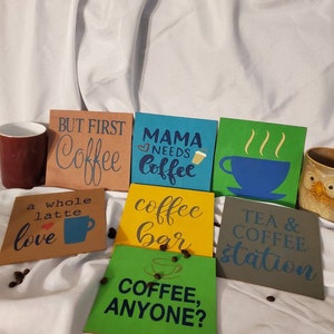 Puede incluir: Una colección de seis letreros de madera con frases sobre el café. Los letreros están pintados en varios colores, incluyendo verde, azul, amarillo, marrón y gris. Los letreros presentan textos como "But First Coffee", "Mama Needs Coffee", "Coffee Bar", "Tea & Coffee Station", "A Whole Latte Love", y "Coffee, Anyone?"