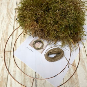 Pu&ograve; includere: Un kit fai-da-te per la creazione di ghirlande con un telaio in metallo color rame, un fascio di muschio verde, spago e una guida stampata. La guida include il testo "Happy wreath making."