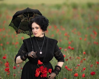 May include: A black dress with a high lace collar, elbow-length sleeves, and a full skirt. The outfit includes sheer black gloves, a silver pendant necklace, and a black lace parasol. A bouquet of bright red poppies is held in the hand.