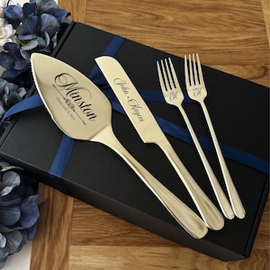 May include: A wedding cake serving set with a cake server, knife, and two forks. The server and knife are engraved with names and a date. The forks are engraved with "Mr" and "Mrs" and an initial. The set is presented on a black box with a blue ribbon.