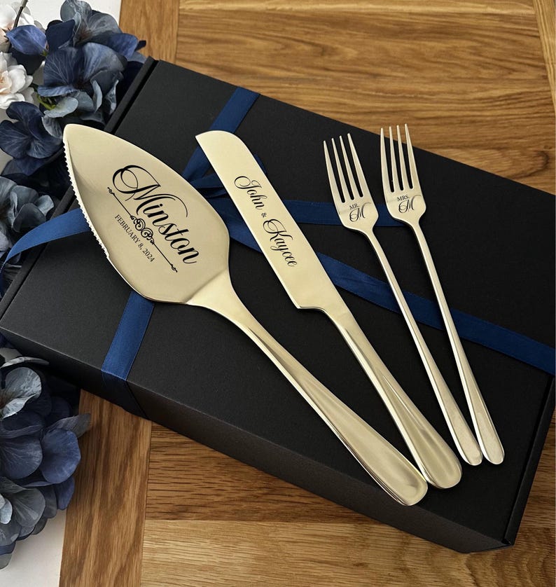 May include: A wedding cake serving set with a cake server, knife, and two forks. The server and knife are engraved with names and a date. The forks are engraved with "Mr" and "Mrs" and an initial. The set is presented on a black box with a blue ribbon.
