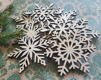 May include: A set of wooden snowflake ornaments, each with a unique design, are arranged on a patterned background. The snowflakes are made of light-colored wood and have a delicate, intricate design.