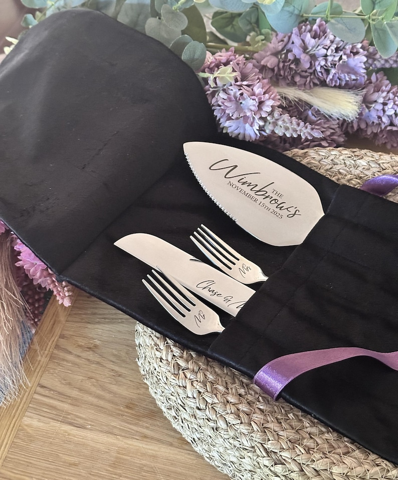 May include: A silver cake server and two forks and a knife set, engraved with names and a date, are displayed in a black fabric holder. The cake server has a serrated edge. The text on the server reads "The Wimbrow's November 15th 2025".