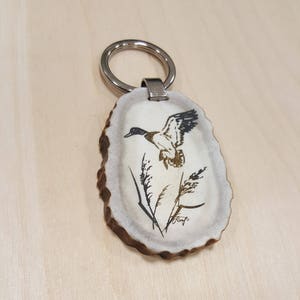 May include: A white antler keychain with a silver ring and a black and white image of a duck in flight.