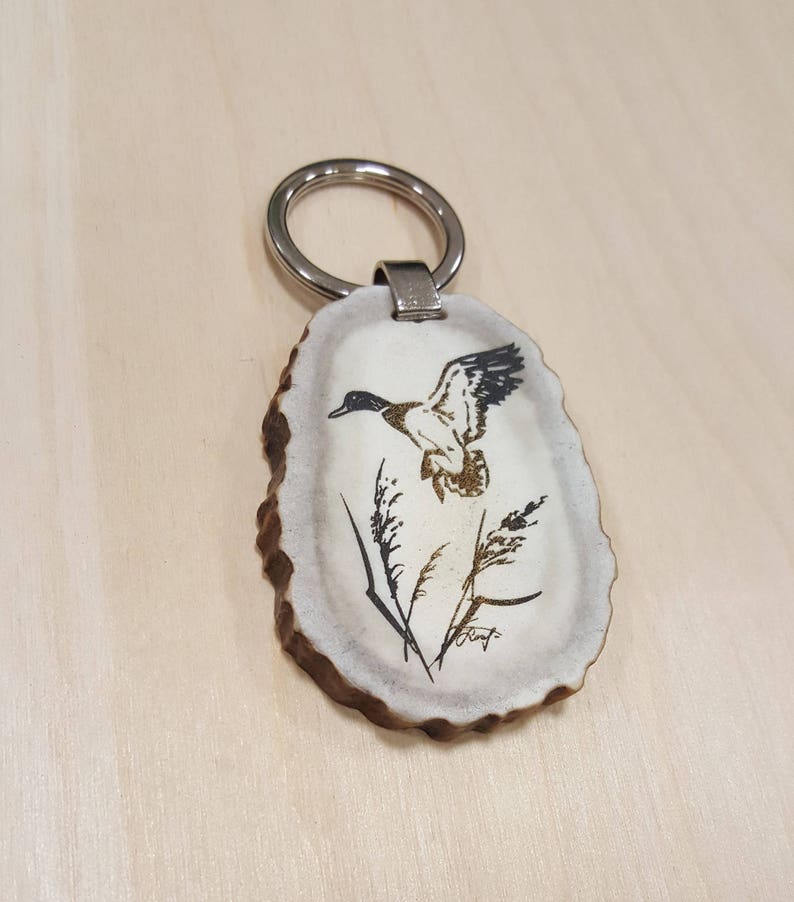 May include: A white antler keychain with a silver ring and a black and white image of a duck in flight.