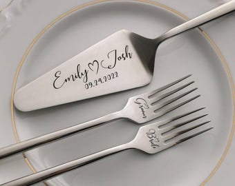 May include: A silver cake server and two forks are displayed on a white plate with a gold rim. The server is engraved with "Emily ♥ Josh" and the date "09.24.2022." The forks are inscribed with "Groom" and "Bride."