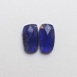 Puede incluir: Dos piedras preciosas rectangulares facetadas de color morado oscuro.