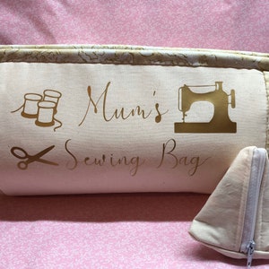 May include: A beige sewing bag with gold embroidery that says "Mum's Sewing Bag". The bag has a zipper and two handles. There is a small beige zippered pouch in front of the bag.
