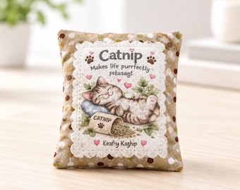 May include: A rectangular fabric catnip toy featuring a tan and white polka dot border. The center panel displays a sleeping tabby cat illustration with the text Catnip Makes life purrfectly pleasant and Leafy Kathip, accented by small pink hearts.