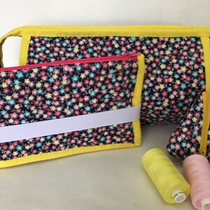 May include: Three zippered pouches with a floral print and yellow trim. The pouches are made of fabric and have a white elastic band on the larger pouch. There are also three spools of thread in yellow, pink, and blue.