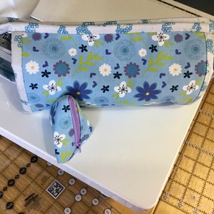 May include: A blue and white floral fabric zippered pouch with a smaller matching pouch. The larger pouch has a handle and is lying on a white surface.