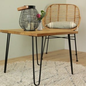 May include: A wooden coffee table with black hairpin legs. The table is sitting on a white rug and has a wicker chair next to it.