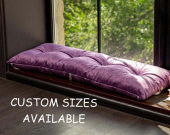 Pode incluir: Um assento de janela roxo com textura de veludo macio está em um peitoril de janela com um urso de pelúcia e livros. O texto "CUSTOM SIZES AVAILABLE" está impresso no chão.