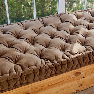 May include: A brown tufted window seat cushion with a book on top. The cushion is made of a soft, plush fabric and has a thick, comfortable padding.